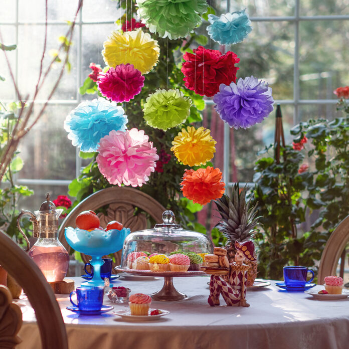 Colorful tissue paper pom poms hanging above a tea party table in a bright room