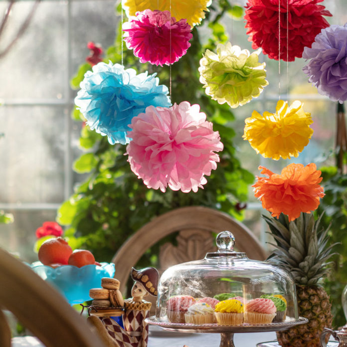 Colorful tissue paper pom poms hanging above a party table